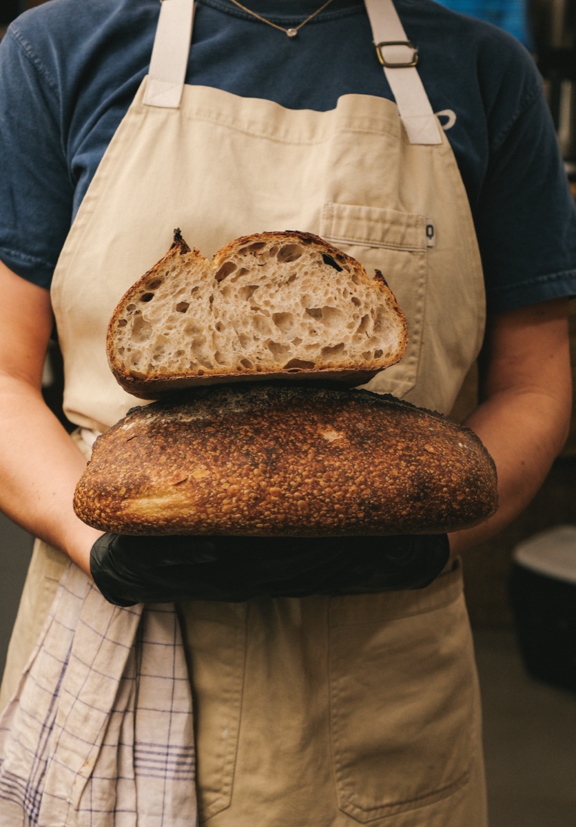 Baker holding freshly baked sourdough loaf with open crumb at Santo Bakehouse Madrid
